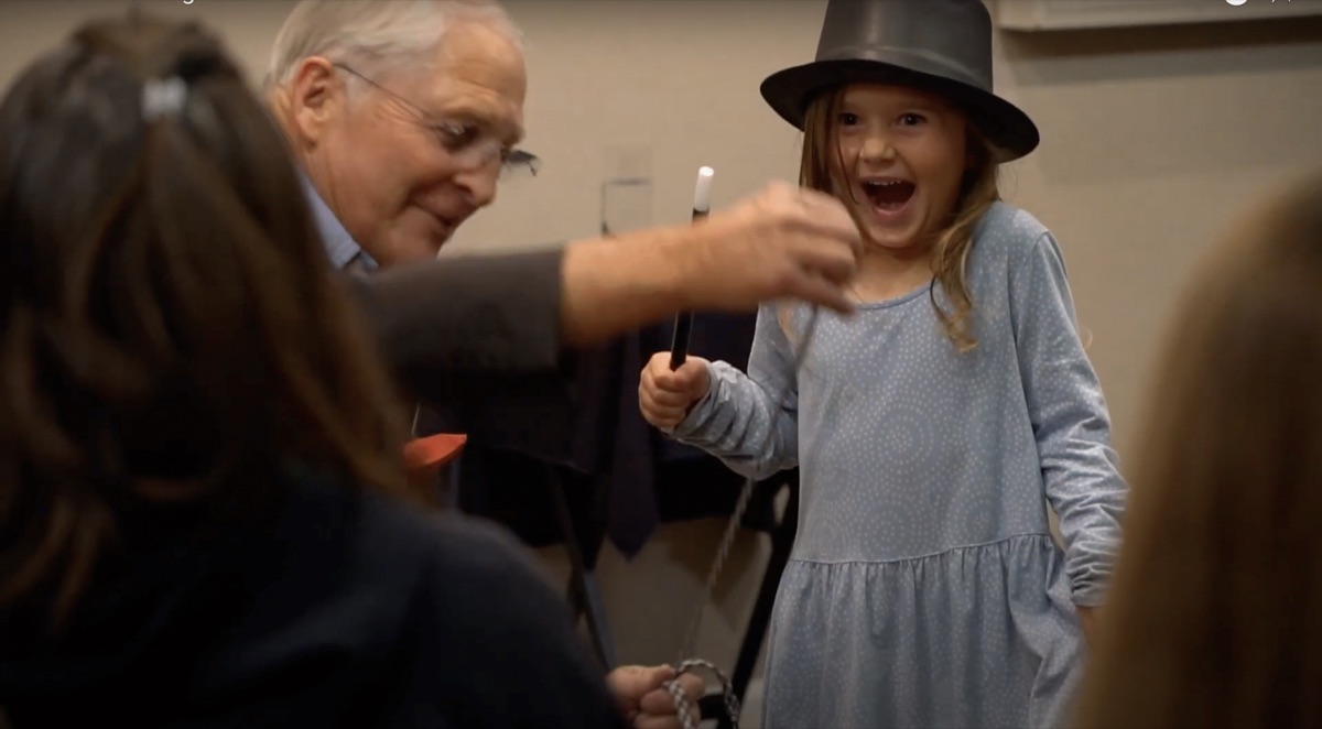 A young guest in Jim's top hat, delighted, holding the magic wand
